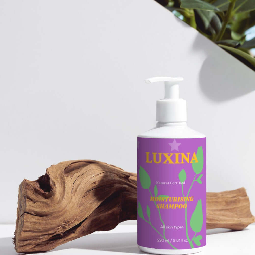 Luxina shampoo bottle with a purple label on a white surface with greenery in the background