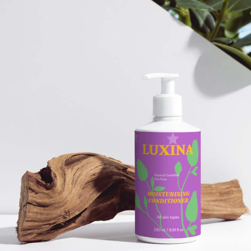 Luxina conditioner bottle with a purple label on a white surface with a plant in the background